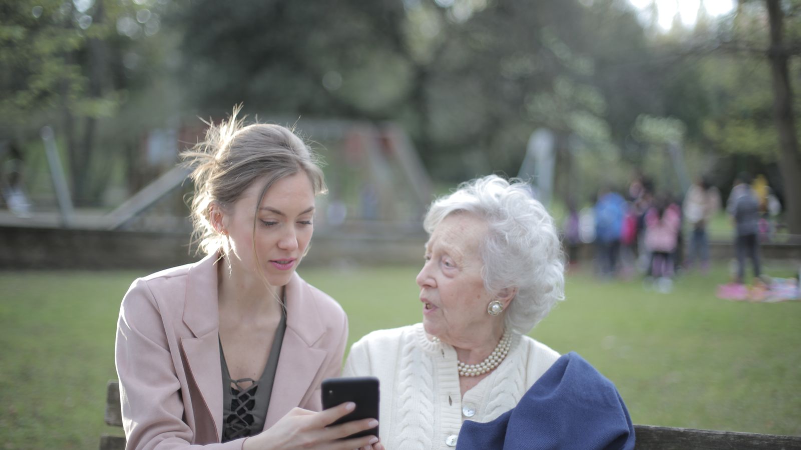 An adult daughter teaching her elderly mother to use a smartphone in a garden