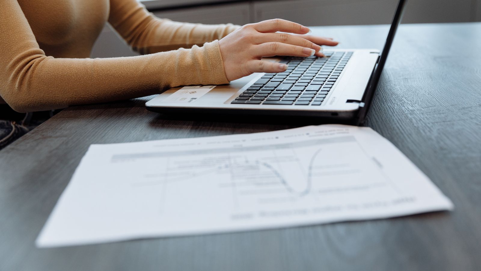 Hands typing on a laptop at a desk beside documents, the process of exporting family lineage records