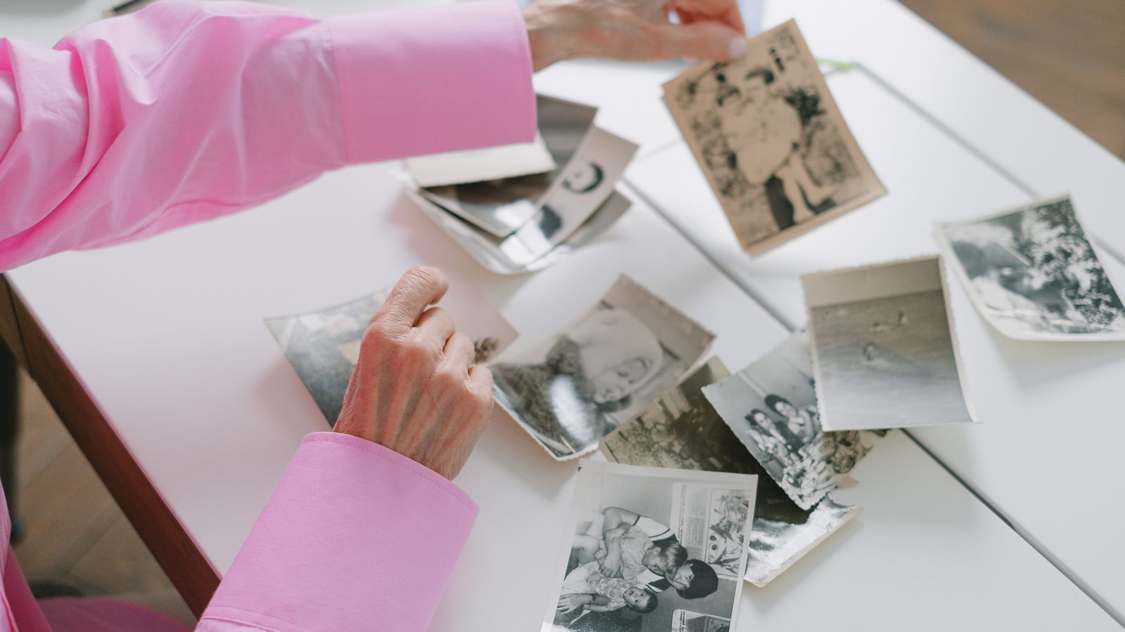 A woman leafing closely through old family photographs while sorting a heritage picture collection