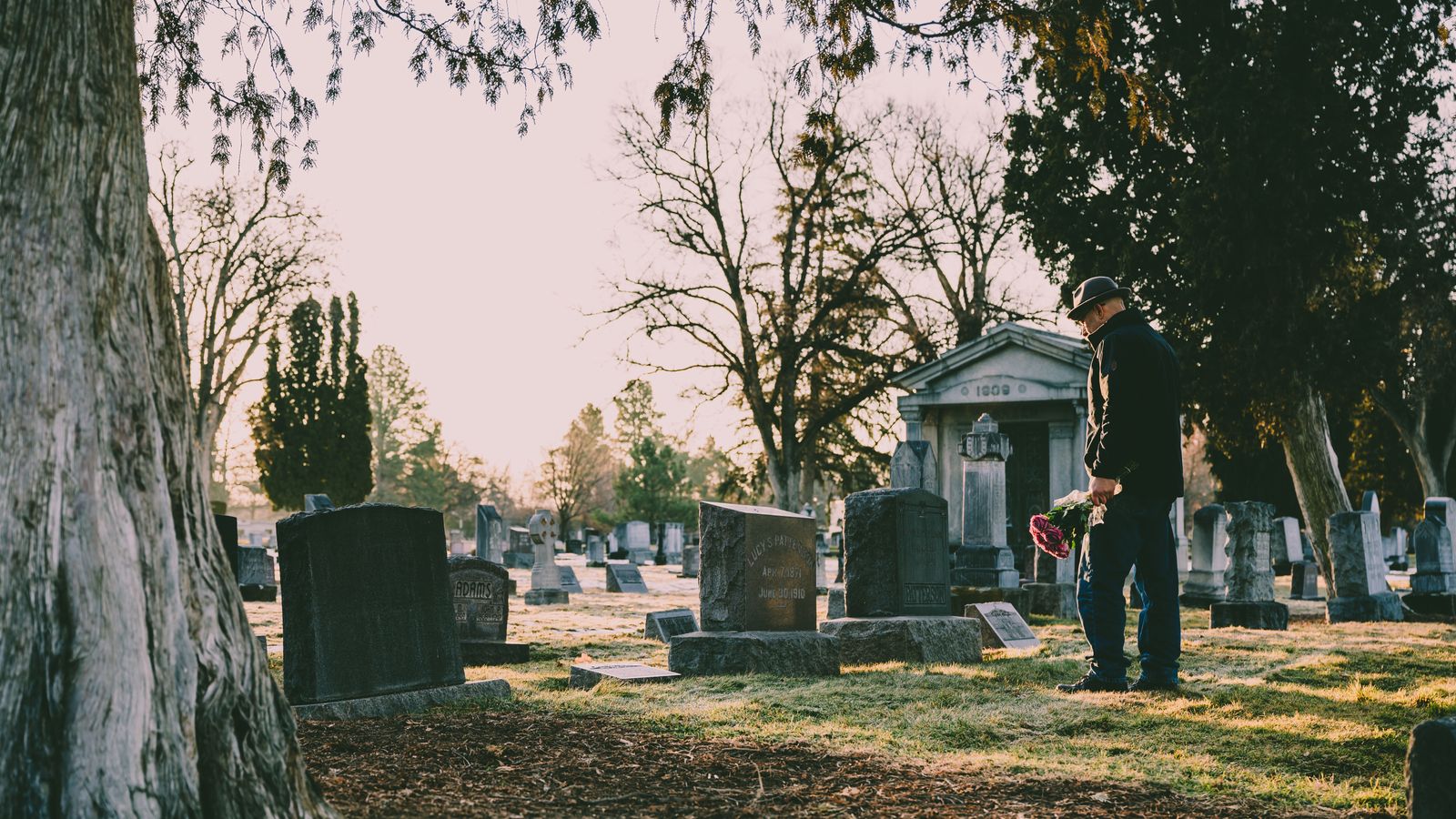 A person standing with flowers in a quiet cemetery while visiting a family member's grave