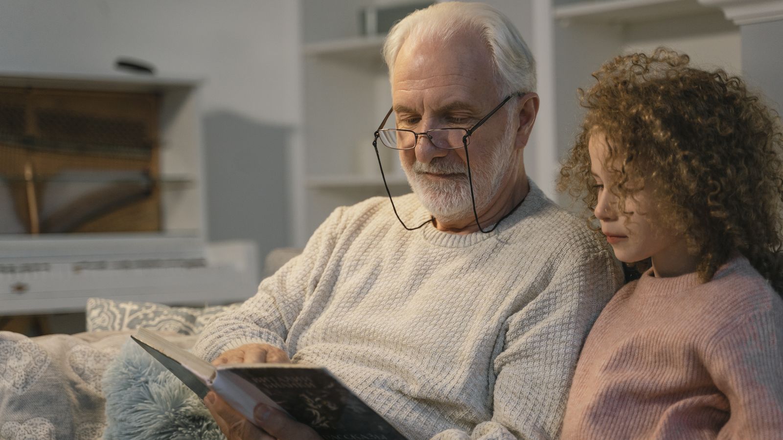 An elderly man reading at home with his granddaughter, the moment when family stories are gathered from the oldest generation