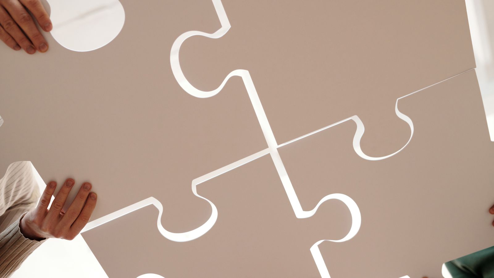 Several hands holding large puzzle pieces and fitting them together, illustrating the merging of two family trees