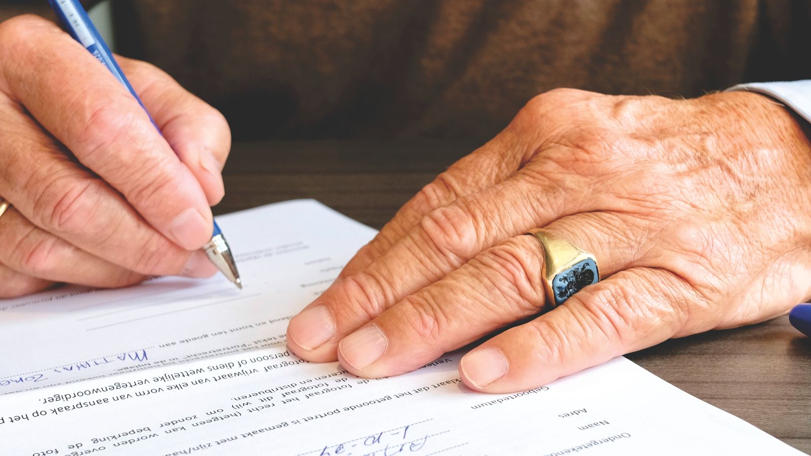 The hands of an elderly person signing an official legal document with a pen at a table
